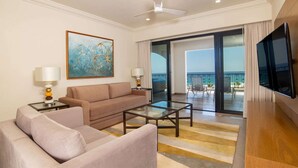 Ein Hotelzimmer mit Sofa, Couchtisch, Fernseher, einem Gemälde und einem Balkon mit Aussicht.