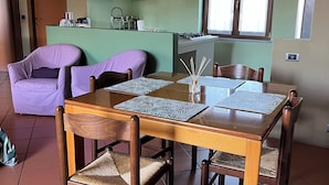 A dining area with a wooden table and chairs, a kitchen in the background, and a window with blinds. - A Getaway in Nature: Lakes & Golf (Bogogno)
