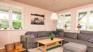 Una habitación acogedora con un sofá seccional gris, una mesa de centro de madera y un ventanal con vistas a zonas verdes.