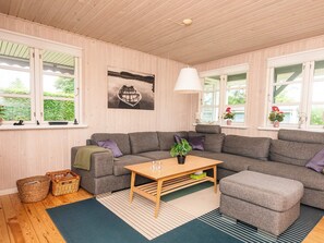 A cozy room with a grey sectional sofa, a wooden coffee table, and a large window with a view of greenery. - 6 Person Holiday Home in Hadsund (Hadsund)