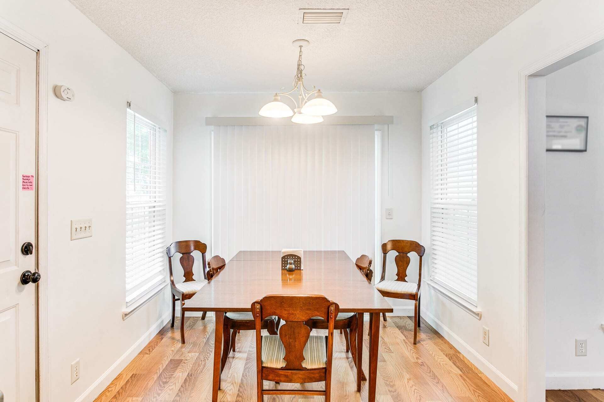 Une salle à manger avec une table et des chaises en bois, des murs blancs et un luminaire au plafond.