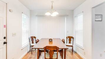 Une salle à manger avec une table et des chaises en bois, des murs blancs et un luminaire au plafond.