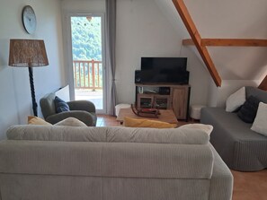 A living room with a sofa, a television, a lamp, and a view of the outdoors.
