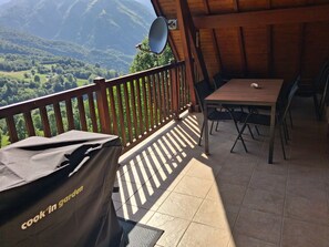 A balcony with a table and chairs, a satellite dish, and a view of green hills.