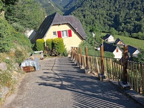 Un chemin de campagne menant à une maison avec un toit en pente et des volets rouges.