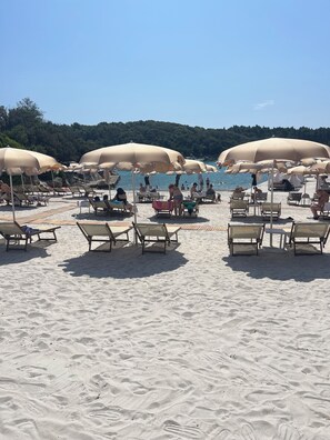 Ein Strand mit Liegestühlen und Sonnenschirmen, eine Holzterrasse und Blick aufs Meer.