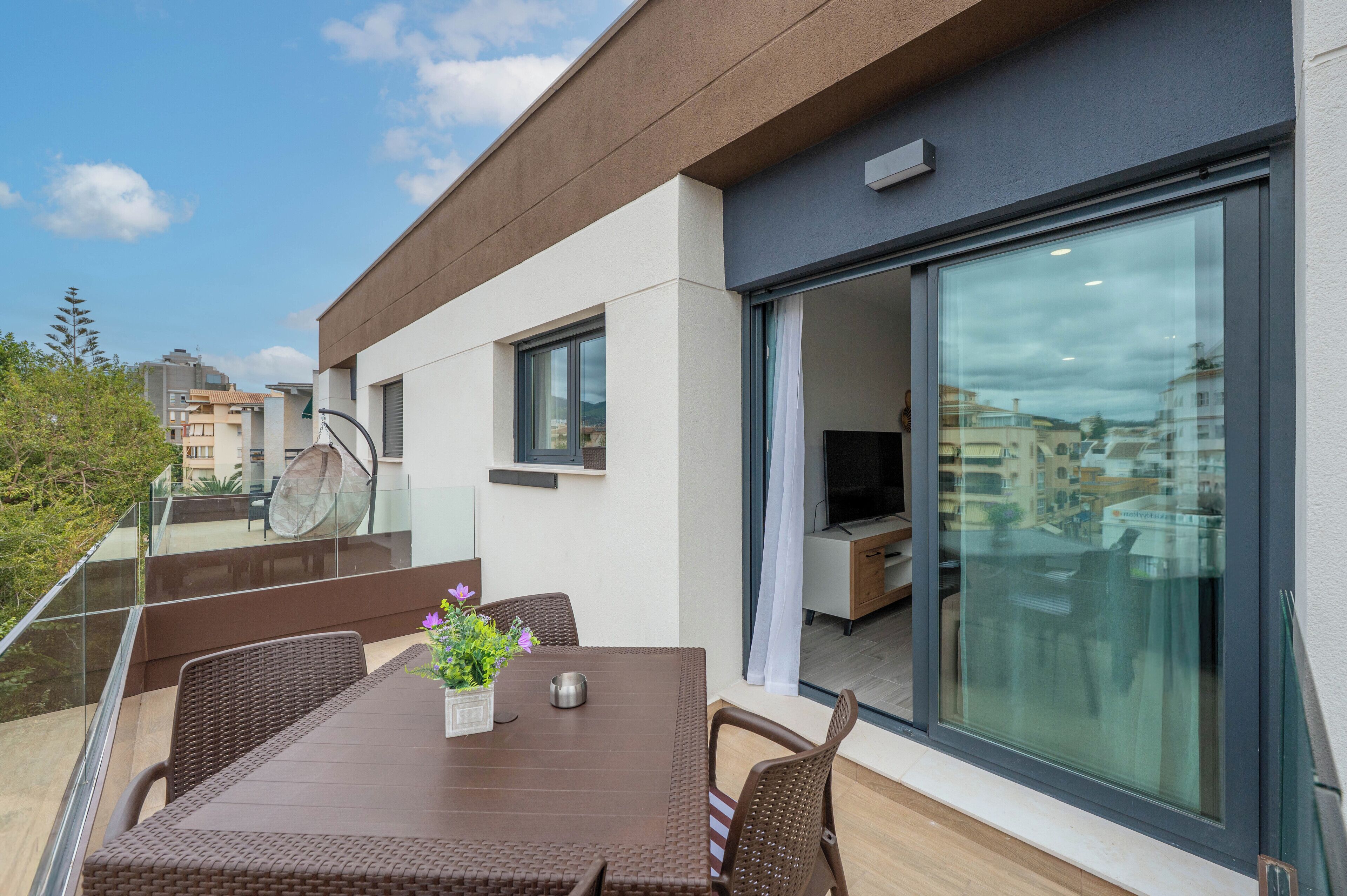 A modern balcony with a glass door, a dining table with chairs, and a potted plant.