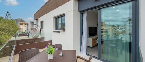 A modern balcony with a glass door, a dining table with chairs, and a potted plant.