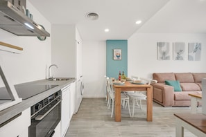 A modern kitchen with a built-in oven, a dining area with a wooden table and chairs, and a living area with a sofa and a blue accent wall. - LXR Meninas 2-Bedroom Apartment Near the Sea (Fuengirola)