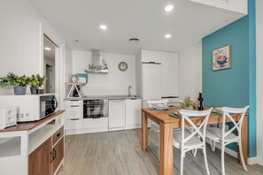 A modern kitchen with white cabinetry, a wooden dining table, and white chairs. - LXR Meninas 2-Bedroom Apartment Near the Sea (Fuengirola)