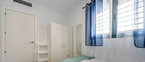 A bedroom with two beds, a wardrobe, a mirror, and a window with curtains.