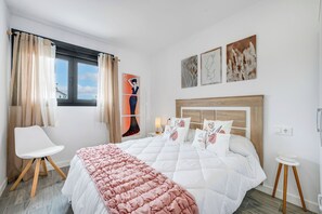 Un dormitorio con cama, una silla, un ventanal con cortinas y decoración en la pared.
