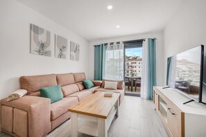 A modern living room with a sofa, a coffee table, a TV, and a balcony with curtains. - LXR Meninas 2-Bedroom Apartment Near the Sea (Fuengirola)
