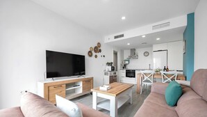 A modern living room with a TV, sofa, coffee table, and kitchen in the background. - LXR Meninas 2-Bedroom Apartment Near the Sea (Fuengirola)