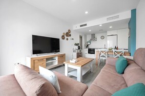 A modern living room with a TV, sofa, coffee table, and kitchen in the background. - LXR Meninas 2-Bedroom Apartment Near the Sea (Fuengirola)