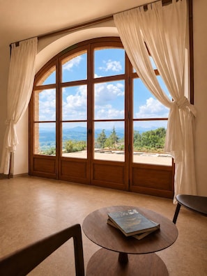 A room with a large arched window, a round table with a book, and a chair. - Villa Santa Maria dell'Olmo (MORESCO)