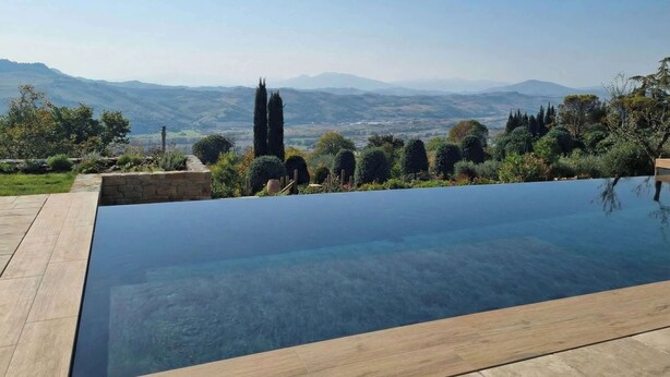 A clear view of a swimming pool with a stone border and a wooden deck, surrounded by well-maintained landscaping and distant mountains. - Villa Santa Maria dell'Olmo (MORESCO)