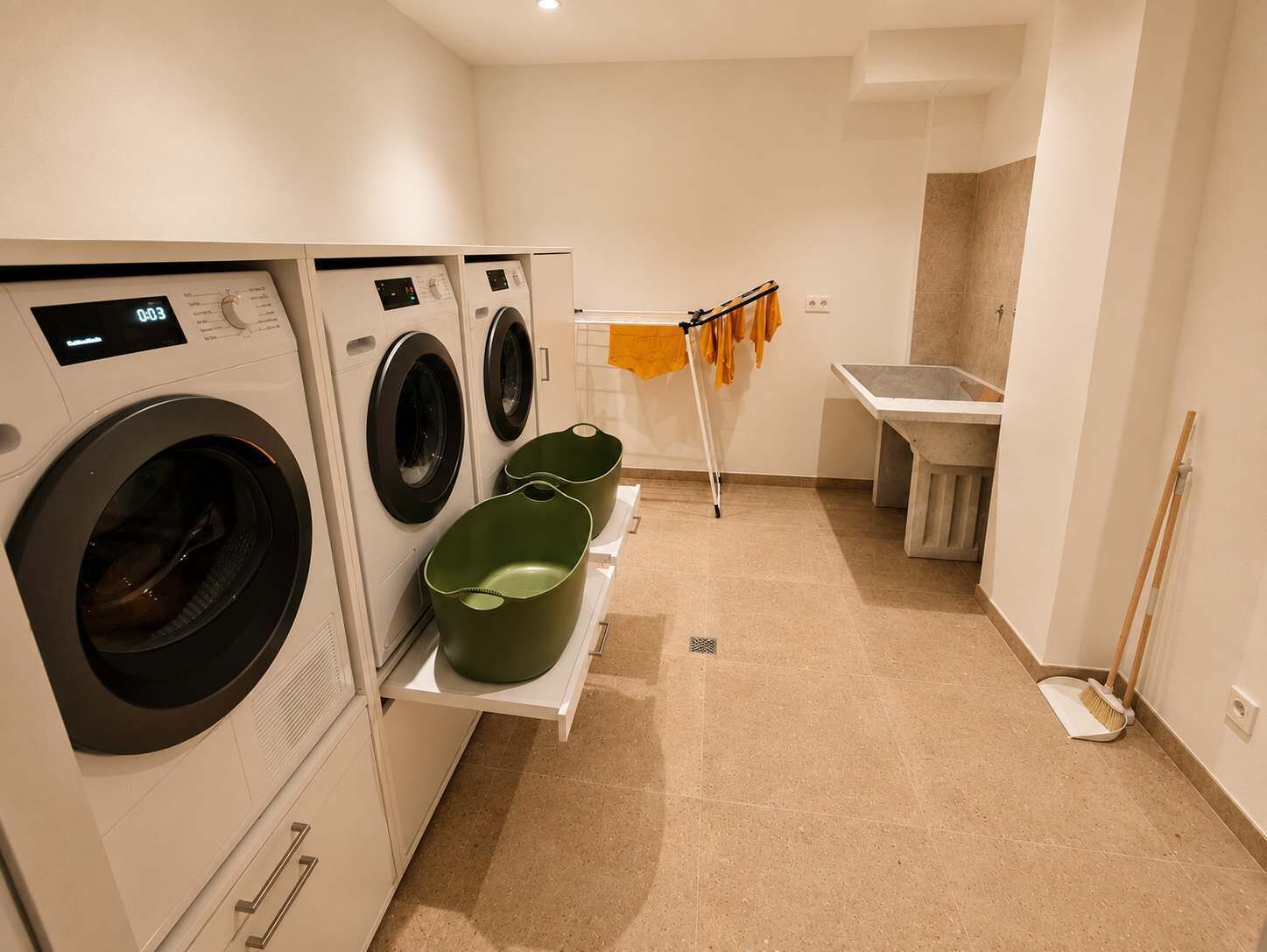 A laundry area with two washing machines, a drying rack, and a sink.