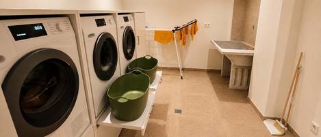 A laundry area with two washing machines, a drying rack, and a sink.