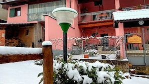 Um edifício cor-de-rosa com varanda, um poste de luz e plantas cobertas de neve.