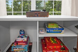 Une étagère avec divers jeux de société, une radio et une fenêtre donnant sur des arbres.