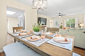 Un coin repas avec une table en bois dressée pour six personnes, un téléviseur au-dessus de la cheminée et un canapé vert en arrière-plan.