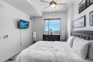 Ein Schlafzimmer mit einem Bett, einem Fernseher, einem Deckenventilator, einem Fenster mit Blick und Kunstwerken an den Wänden.