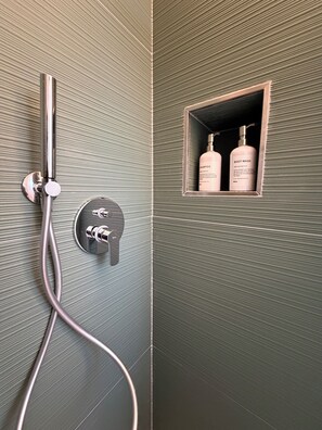 A shower with a handheld showerhead and a wall-mounted control panel. There is a small shelf with two bottles labeled 'BODY WASH' and 'SHAMPOO'. - Staying in the vacation home you can experience the magic of Salento Greece (Castrignano De' Greci)