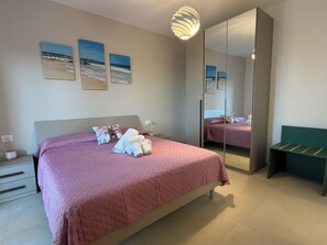 Ein Schlafzimmer mit einem Bett, Kissen, einem Nachttisch, einem Spiegel und Bildern an der Wand.