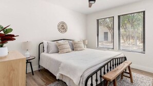 Quarto com cama, ventoinha no teto, mesa de cabeceira com abajur, planta em vaso e janela com persianas.