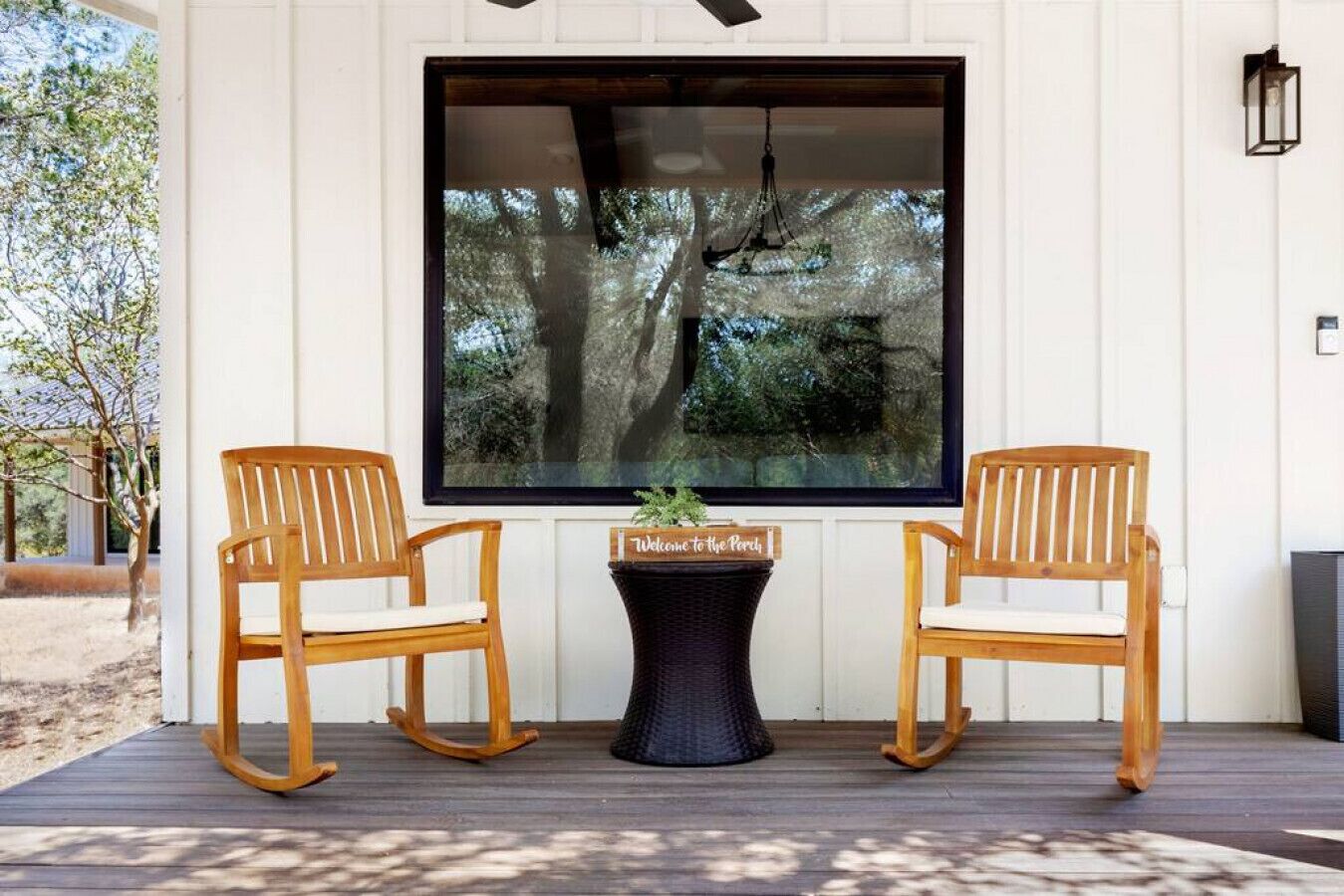 A wooden rocking chair and a table with a sign in front of a large window overlooking trees.