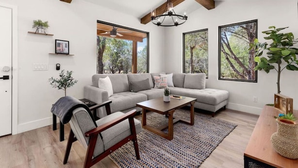 Uma sala de estar moderna com um sofá modular cinza, uma mesa de centro de madeira e uma janela grande com vista para árvores.