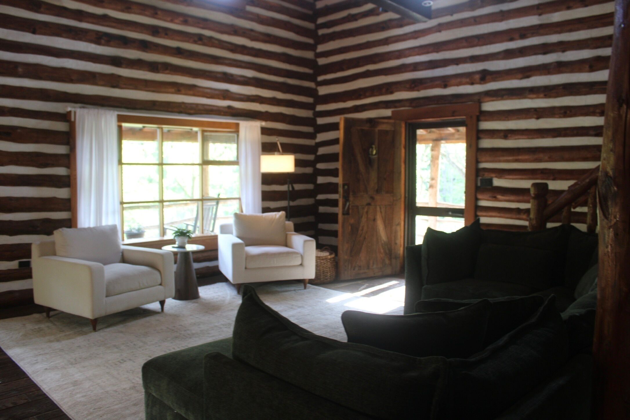 Interno di una baita di legno con camino, due poltrone, un divano e una finestra con tende.