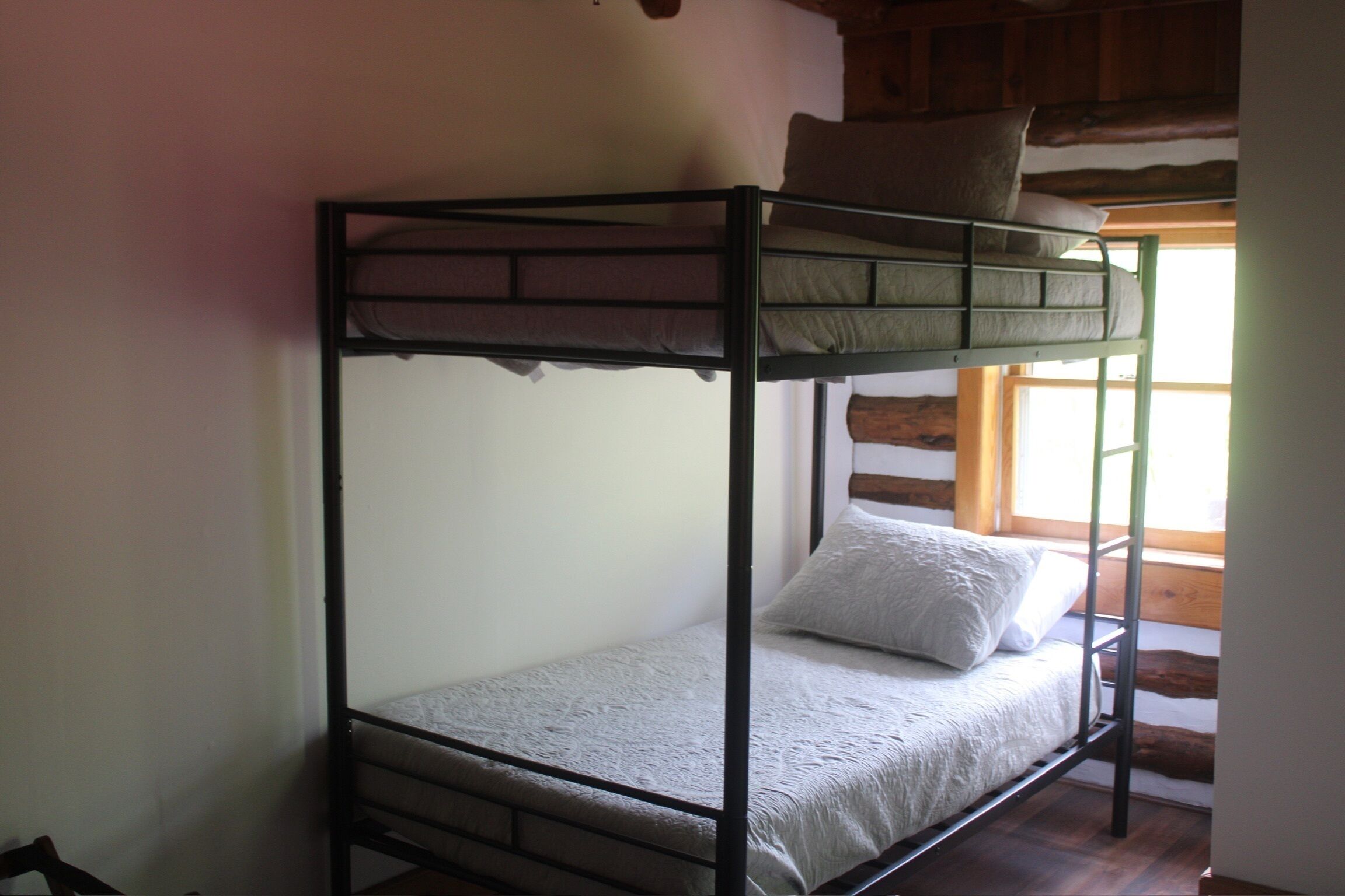 Ein Etagenbett mit Matratze und Kissen, Holzbalken an der Decke und ein Fenster mit Tageslicht.