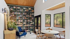 A room with a large bookshelf, a round table with chairs, a blue armchair, and a wooden side table. - Pine Society: 1k Book Library, Elk, yoga or BJJ gym just 5min from PieBar (Pine)