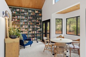 A room with a large bookshelf, a round table with chairs, a blue armchair, and a wooden side table.
