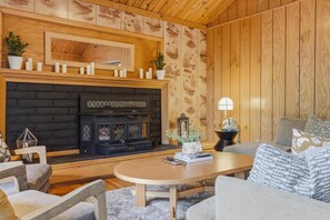 A cozy living room with a fireplace, wooden walls, a sofa, and a coffee table.