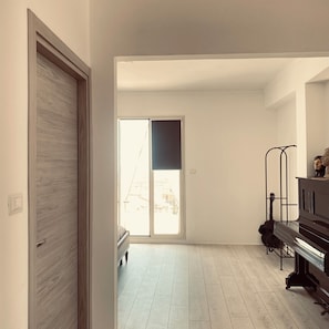 Ein Zimmer mit einem Klavier, einer Bank und einer Tür zu einem hellen Bereich mit Blick.