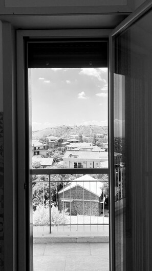 A black and white view through a glass door of a building with a balcony, a stone wall, and a distant landscape with houses and hills. - Etna Rooftop - Panoramic penthouse in Trecastagni with unique view of Etna (Trecastagni)