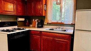 Une cuisine avec des meubles en bois, une cuisinière, une machine à café et une fenêtre donnant sur un paysage verdoyant.