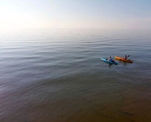 A calm body of water with two kayaks, one blue and one orange, floating.