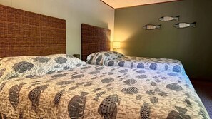 Ein Zimmer mit zwei Betten, einem gewebten Kopfteil, Wandverzierungen mit Fischmotiven und einer Lampe.