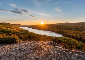Une vallée traversée par une rivière, illuminée par le coucher de soleil, et entourée de collines et d’une végétation luxuriante.