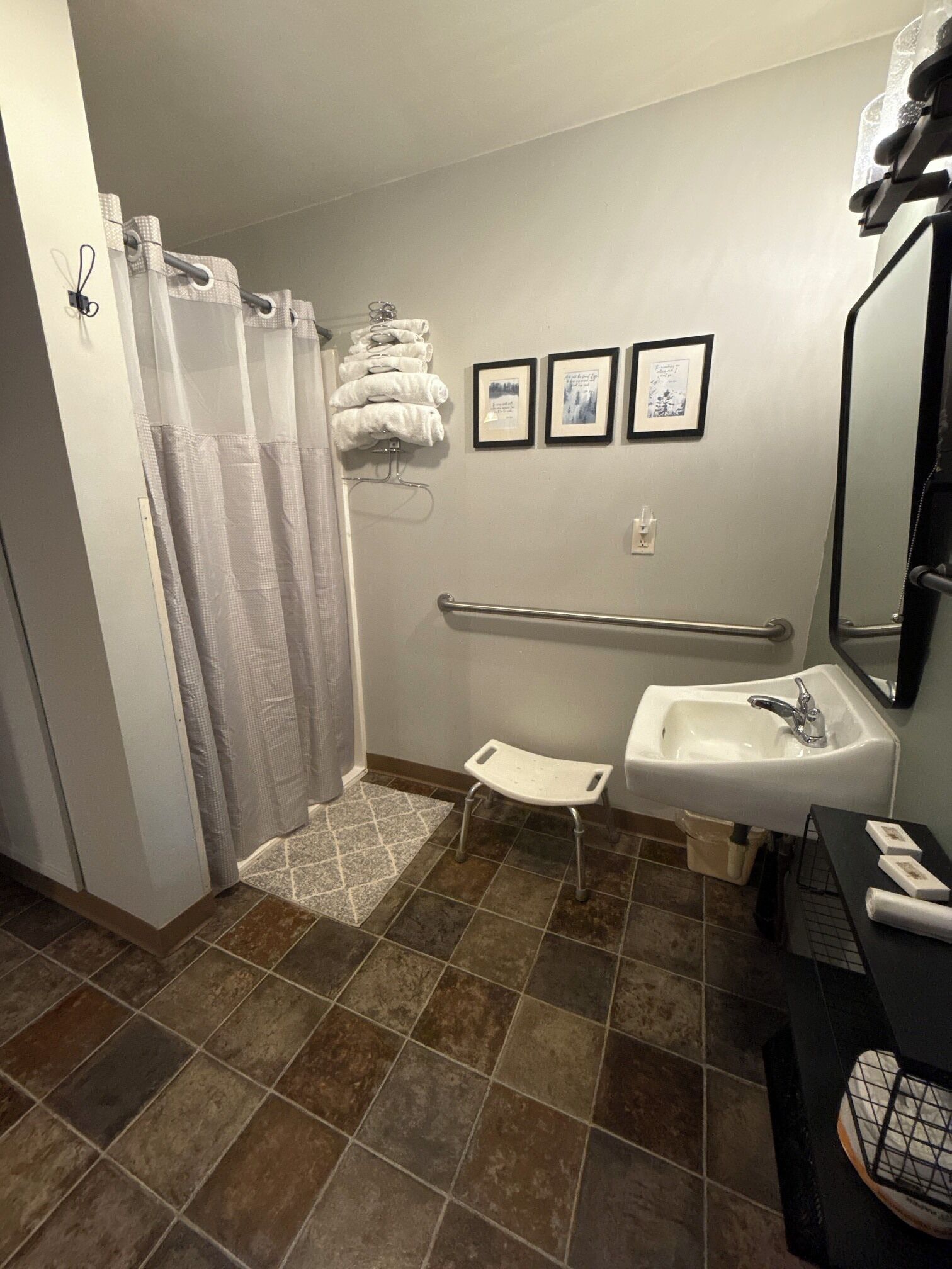 A bathroom with a shower, a sink, a grab bar, and a wheelchair-accessible bench.