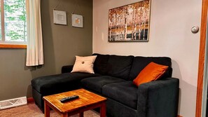 Un salon avec un canapé noir, une table basse en bois et un tableau accroché au mur.