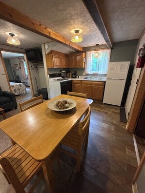 A compact kitchen with wooden cabinets, a dining table with chairs, a stove, and a refrigerator. - Superior View at Miller's Cottages (Ontonagon)