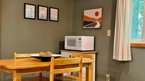 Ein Essbereich mit einem Holztisch und Stühlen, einer Schüssel voller Speisen, einer Mikrowelle und gerahmten Kunstwerken an der Wand.