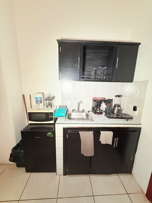 Eine kleine Küche mit einer Mikrowelle, einem Spülbecken und einer Kaffeemaschine.