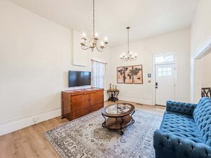 Un soggiorno con divano blu, mobiletti in legno, televisore, lampadario e tappeto decorato.