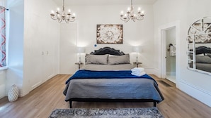 Une chambre à coucher avec un lit, deux lustres, un grand tableau et un miroir.